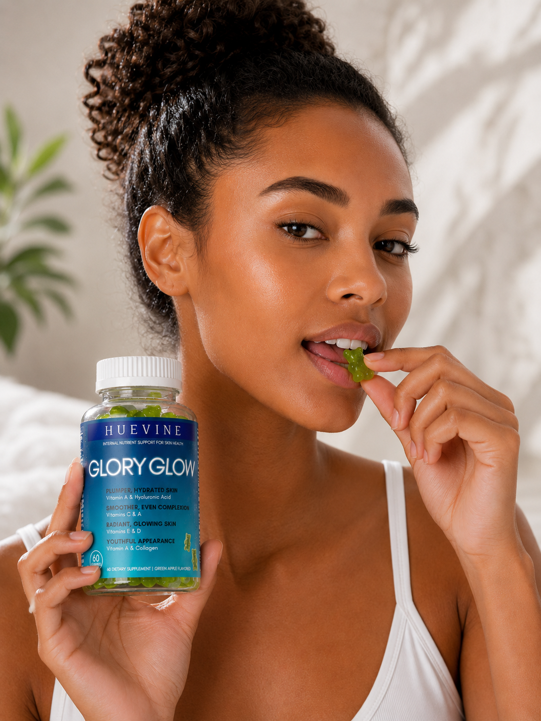 Woman taking a HueVine Glory Glow vitamin gummy while holding the supplement bottle.