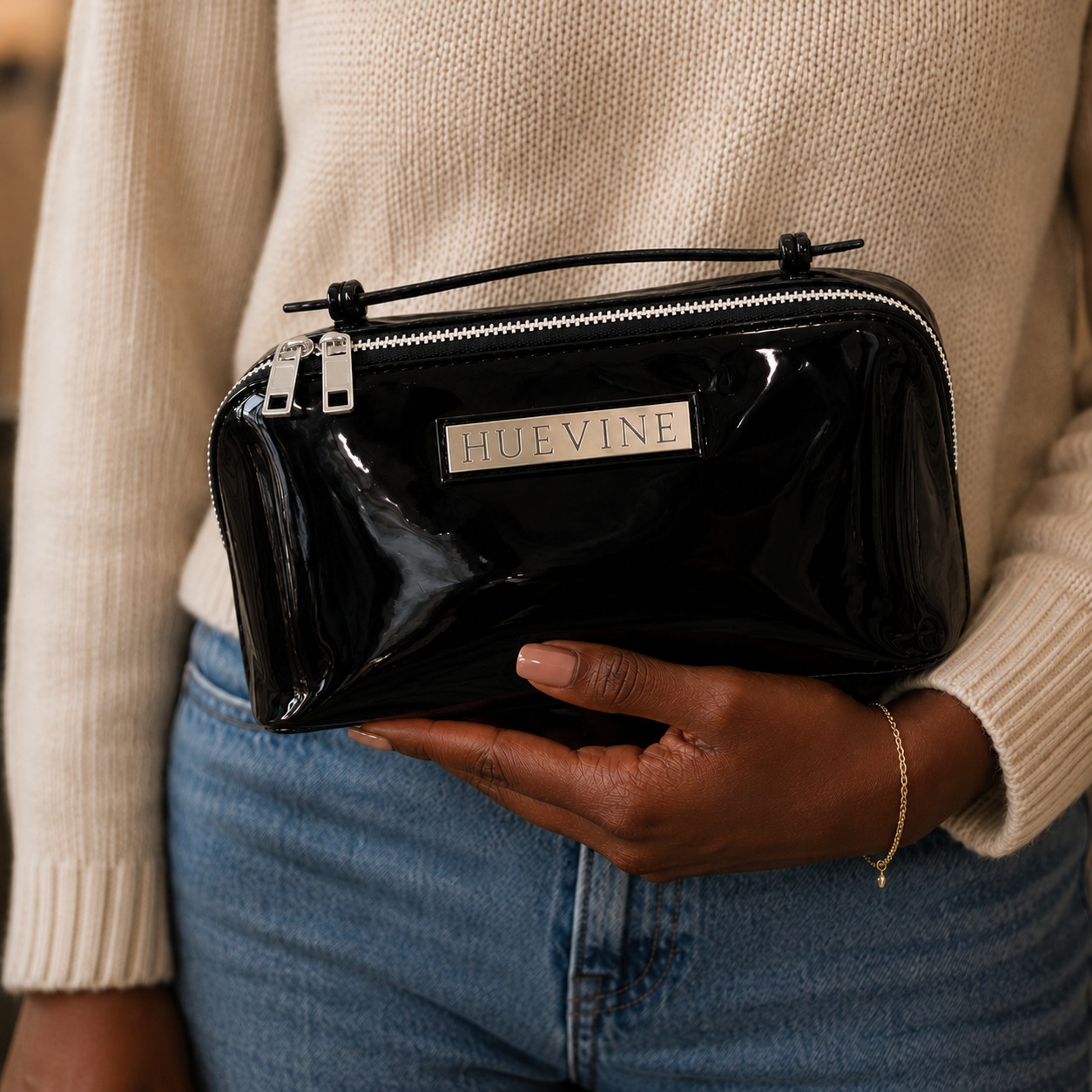 Person holding the HueVine Glow Bag black patent cosmetic case with silver zipper details and glossy finish.