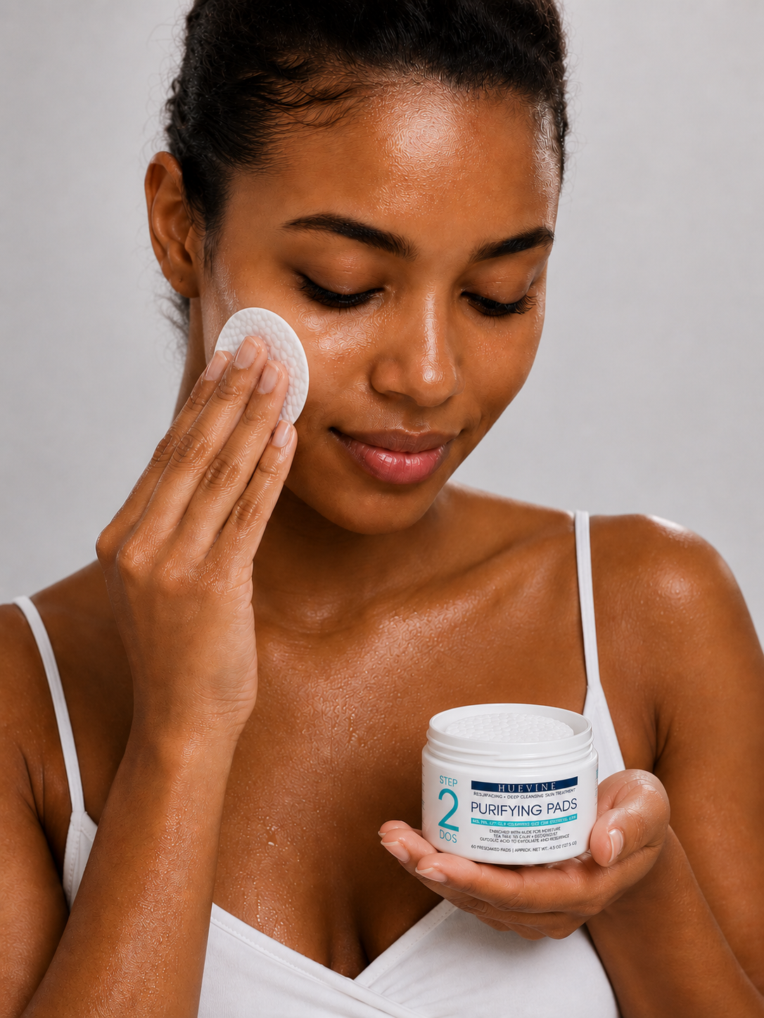 Person using a HueVine Purifying Pad as part of a facial skincare routine while holding the open treatment container.