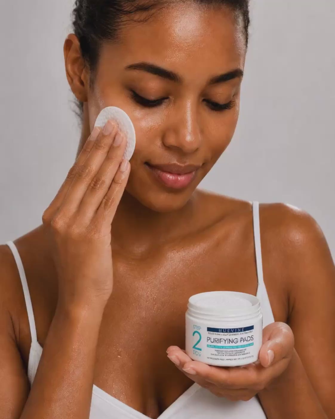 Person demonstrating application of a HueVine Purifying Pad during a facial skincare routine.
